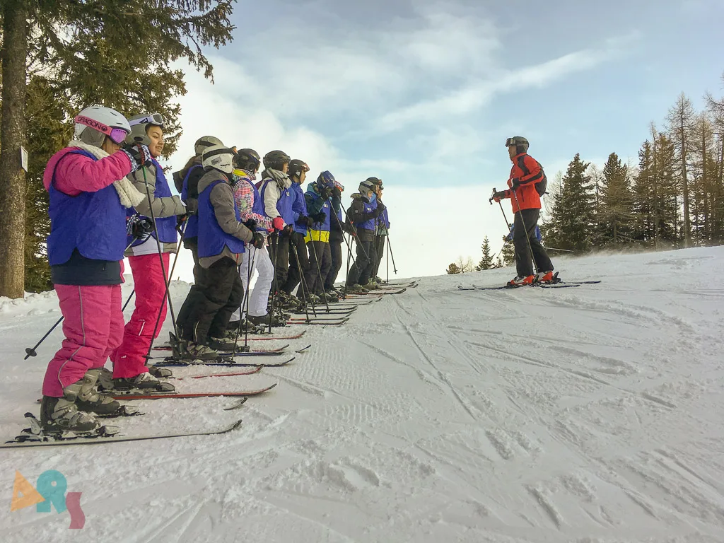 Skigruppe steht in einer Reihe am Pistenrand.